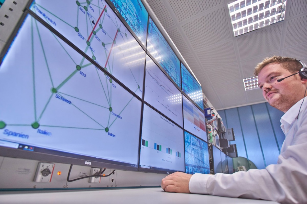 A young man is sitting in front of several screens. He is observing something on one of the screens.