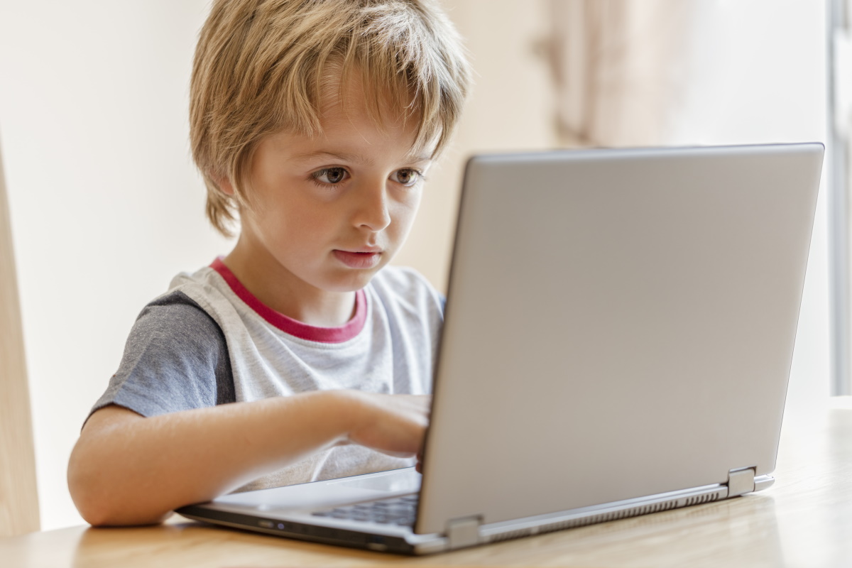 A boy sits in front of a silver laptop.