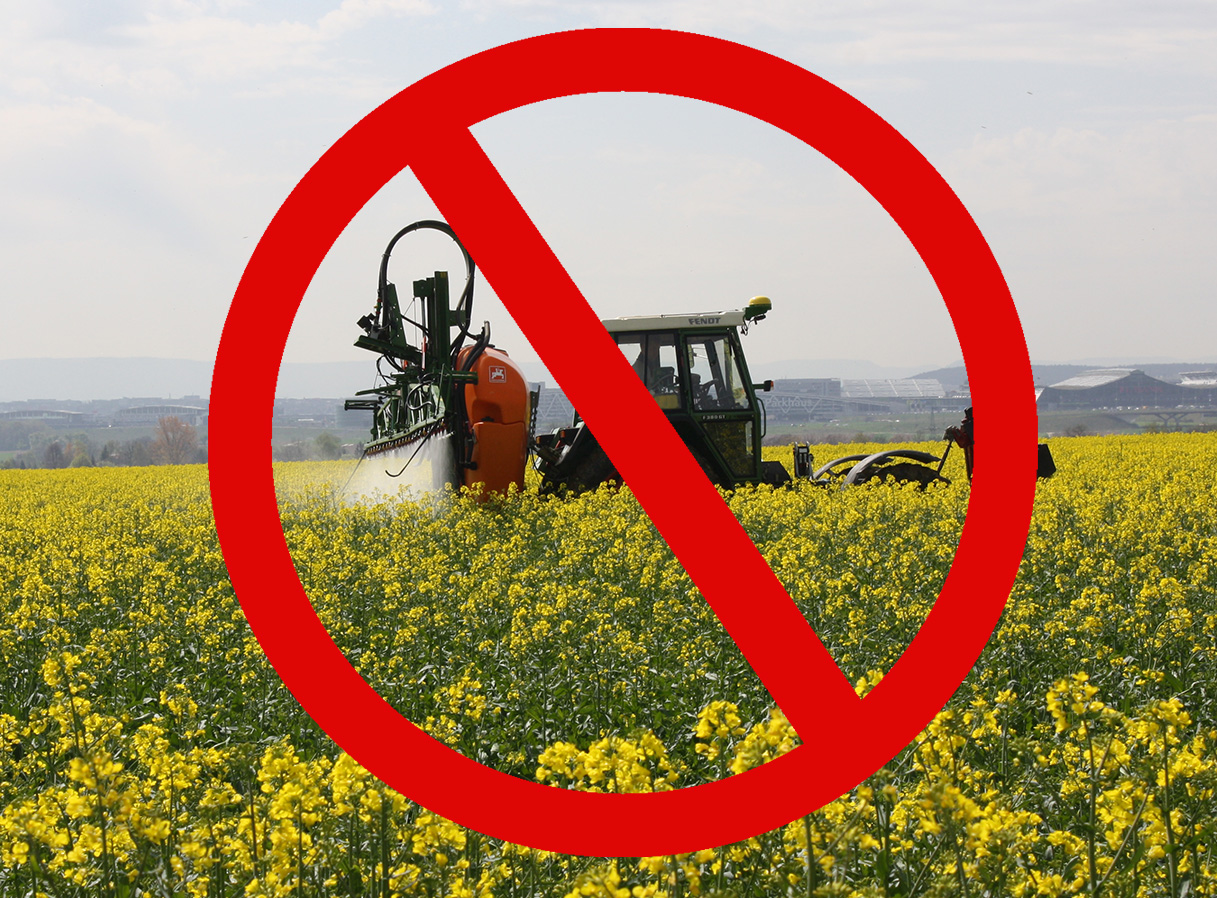 Auf dem Foto ist ein durchgestrichener Traktor zu sehen, der auf dem Feld Pestizide verstreut.
