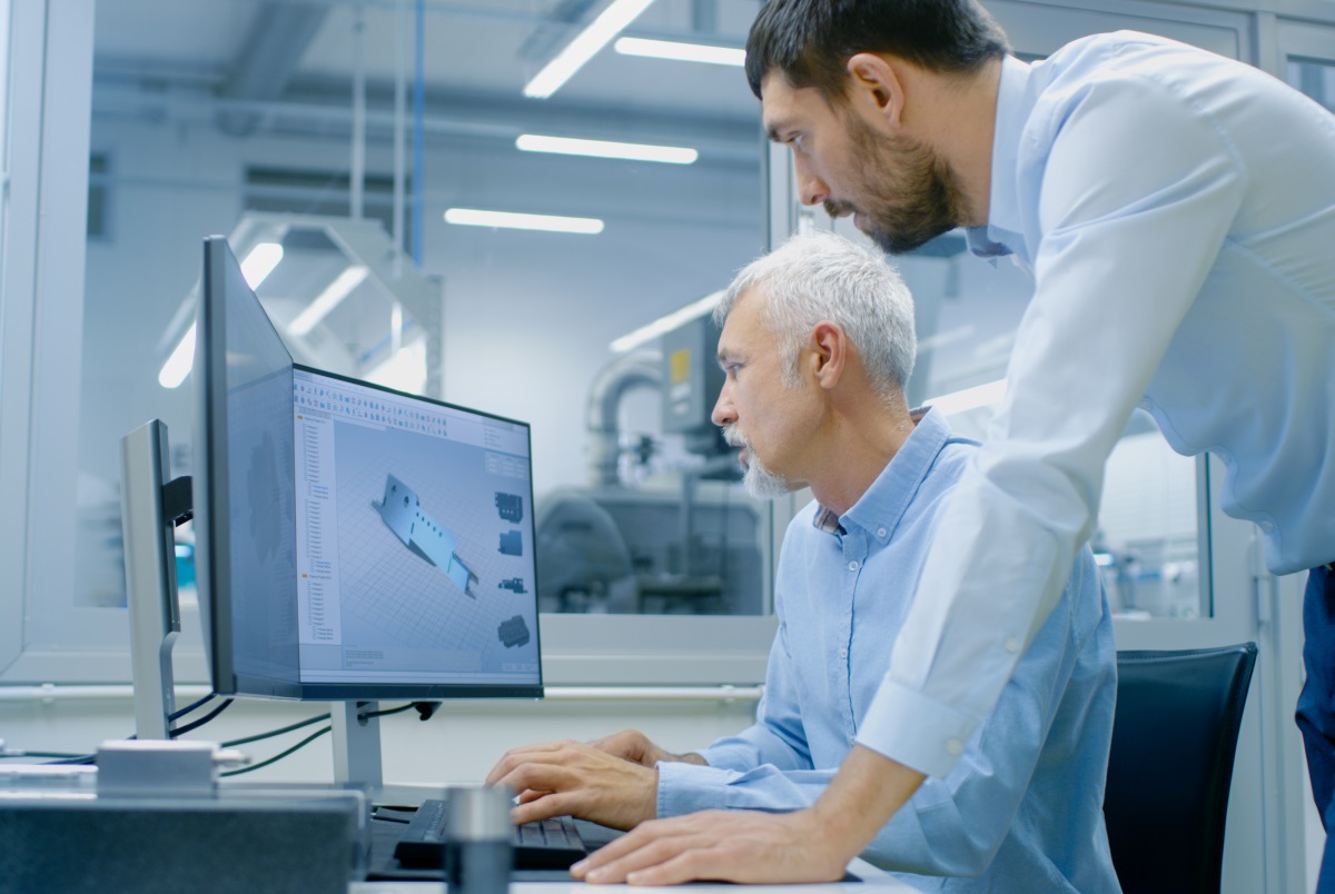 A young man and an older man look at an object together on a screen.